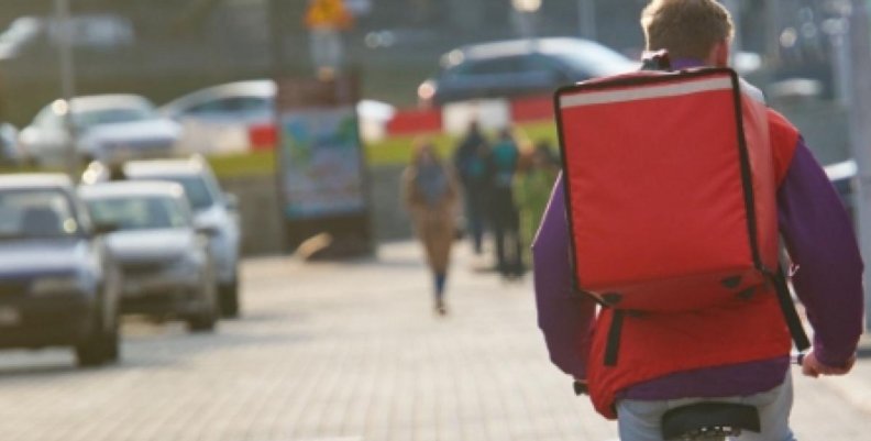 Domiciliario transitando en bicicleta por la ciudad con una mochila cuadrada de color naranja