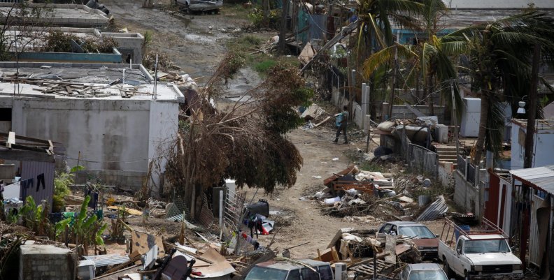 A man carrying a water container walks next to damaged houses after the area was hit by Hurricane Maria in Canovanas