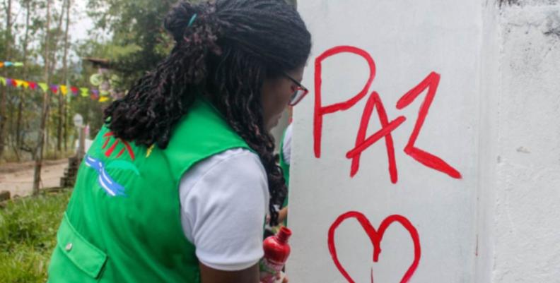 Mujer pintando una pared con la palabra "Paz"