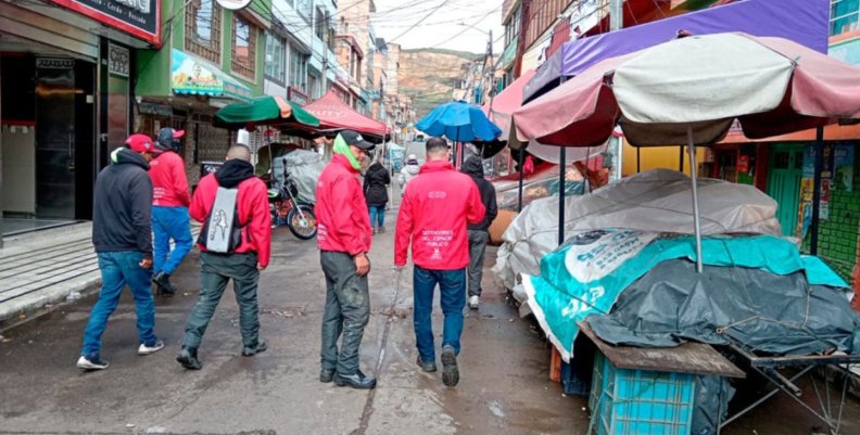 Cuatro hombres con chaquetas rojas caminando sobre una calle llena de puestos de venta ambulante