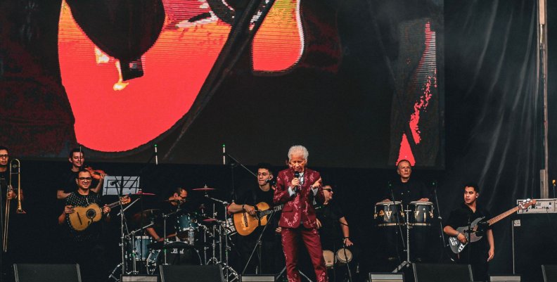 Hombre con traje morado con brillantes, en medio de una tarima con músicos