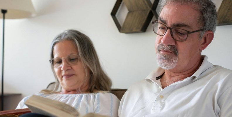 Dos adultos mayores leyendo libros en un sillón