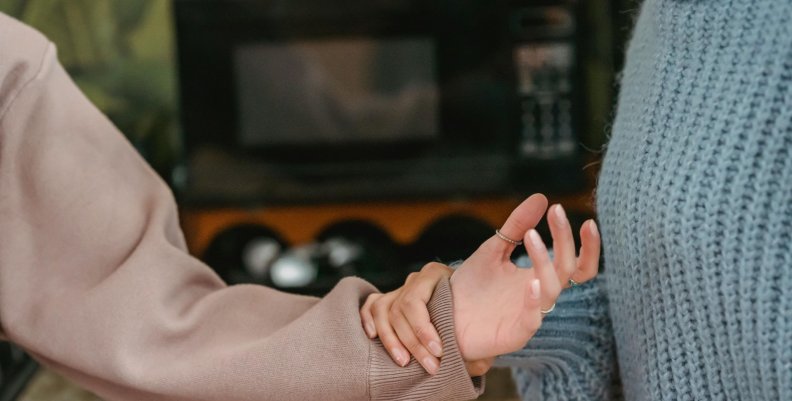 Una persona con saco gris le sostiene la mano a otra con saco café. 