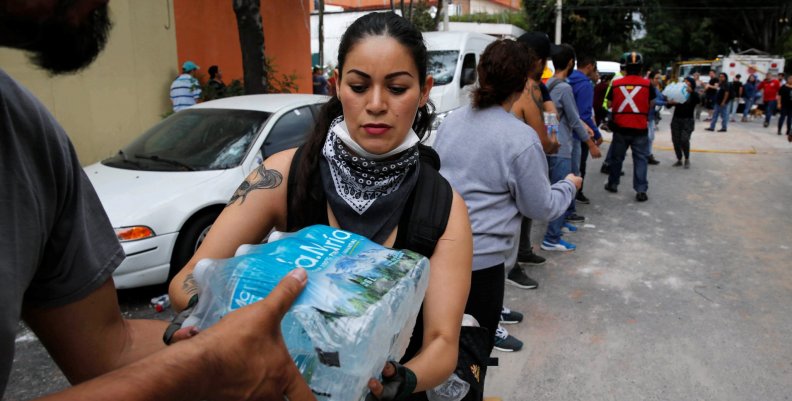 People carry donations of bottled water for rescue workers and victims next to at a collapsed building after earthquake in Mexico City