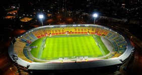 Vista panorámica de un estadio con gradas rojas y amarillas y césped verde en el medio