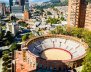 Una plaza de toros con dos torres de edificios detrás