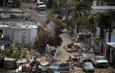 A man carrying a water container walks next to damaged houses after the area was hit by Hurricane Maria in Canovanas