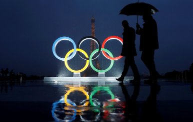 Men walk in the rain under an umbrella next to the Olympic rings after the IOC officially announced that Paris won the 2024 Olympic bid during a ceremony at the Trocadero square near the Eiffel Tower in Paris