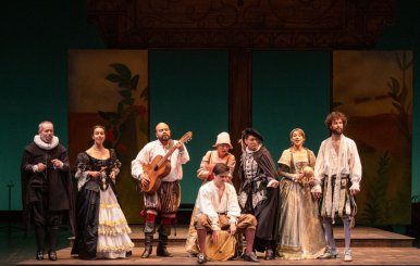 Artistas de teatro reunidos sobre un escenario mirando a la cámara.
