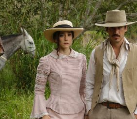 Un hombre y una mujer, vestidos con ropa blanca antigua. Atrás hay un caballo