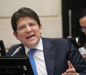 Un hombre con traje negro, camisa blanca y corbata azul en un escritorio